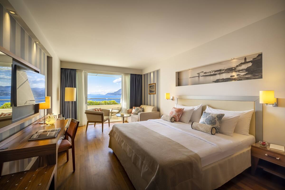 A hotel room with a large bed, a desk, and a view of the sea.
