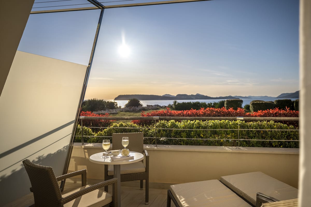 A balcony with a table and chairs, overlooking a scenic view of water and hills.