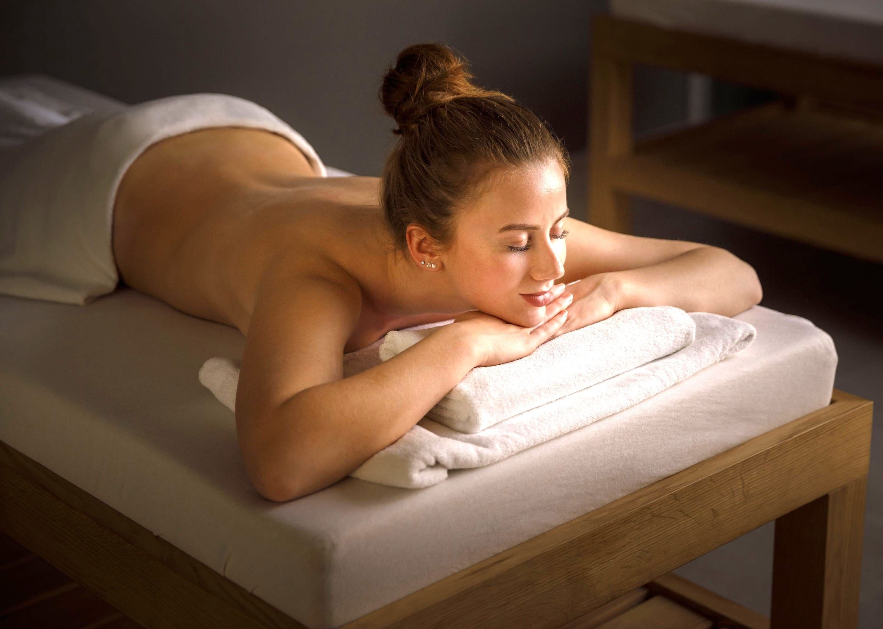 A person lying on a massage table with a towel, in a room with wooden furniture.