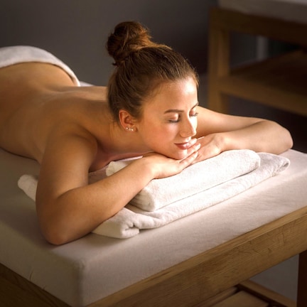 A person lying on a massage table with a towel, in a room with wooden furniture.