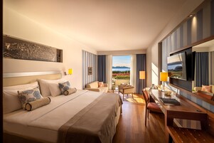 Quarto de hotel com uma cama grande, uma escrivaninha, uma cadeira e vista para o exterior.