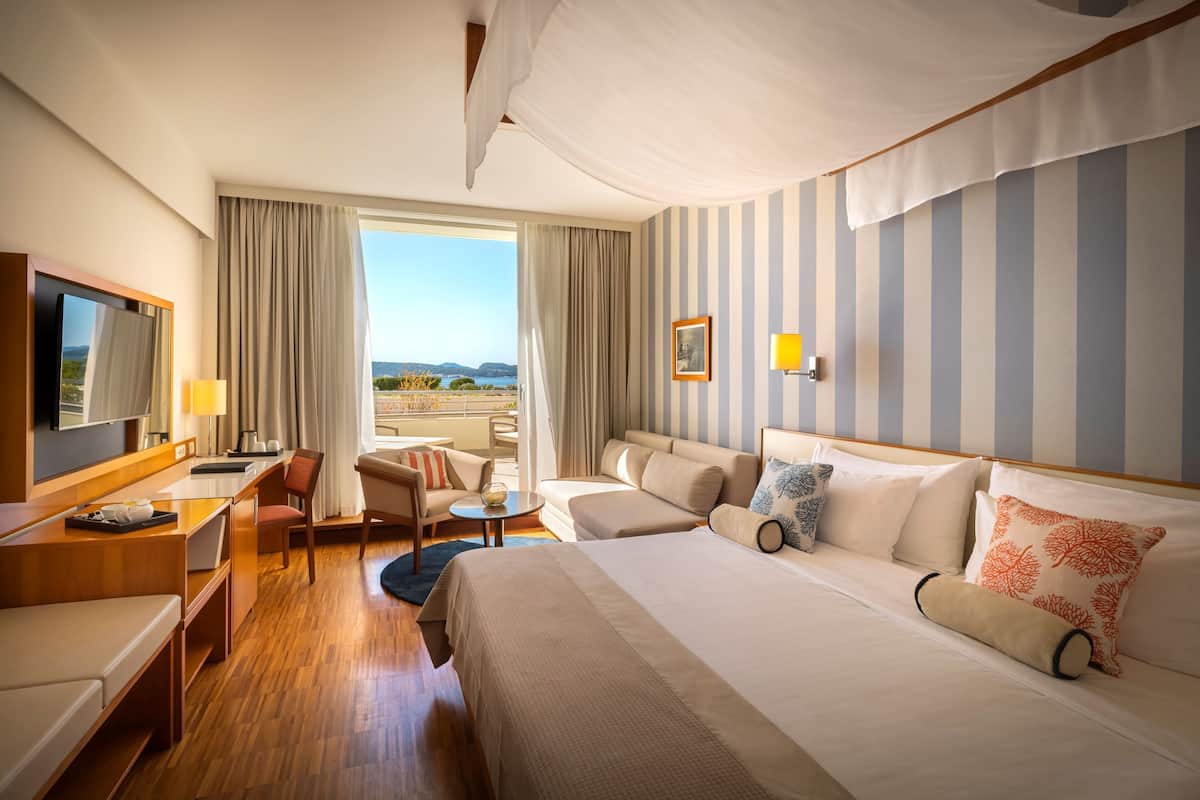 A hotel room with a large bed, a desk, a chair, a sofa, and a TV.