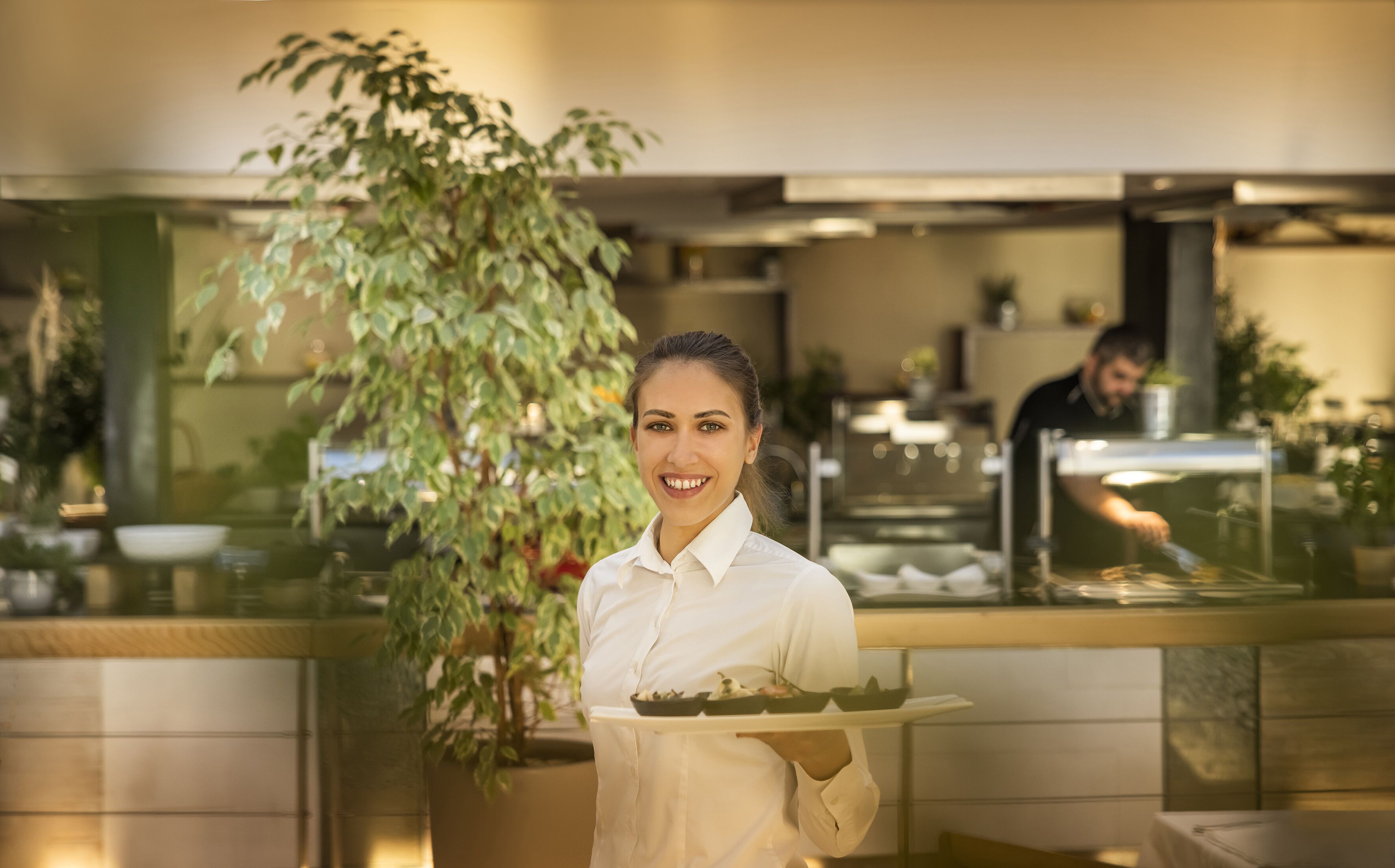 A person holding a tray with food in a restaurant setting with a counter and a plant in the background.