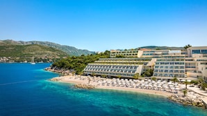 Un hotel frente al mar con varios balcones, una playa con tumbonas y vistas al mar y a las montañas.