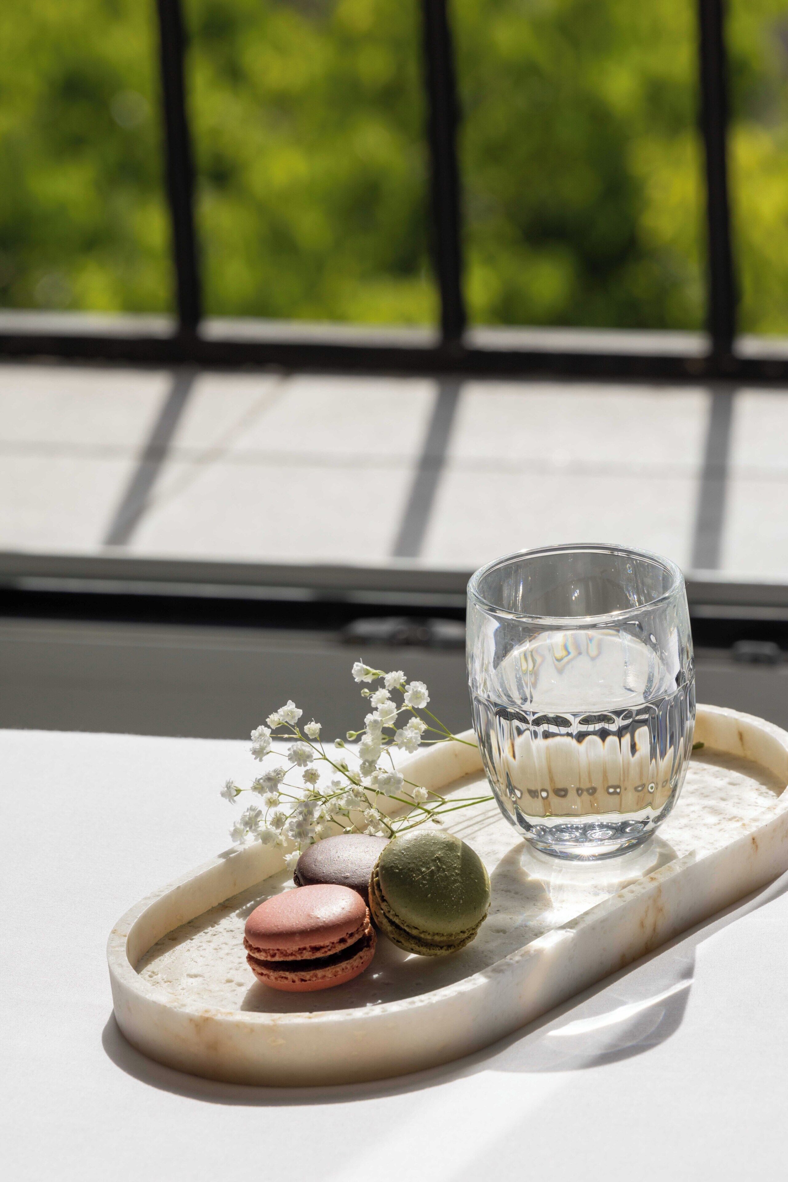 A tray with macarons and a glass of water on a table near a window.