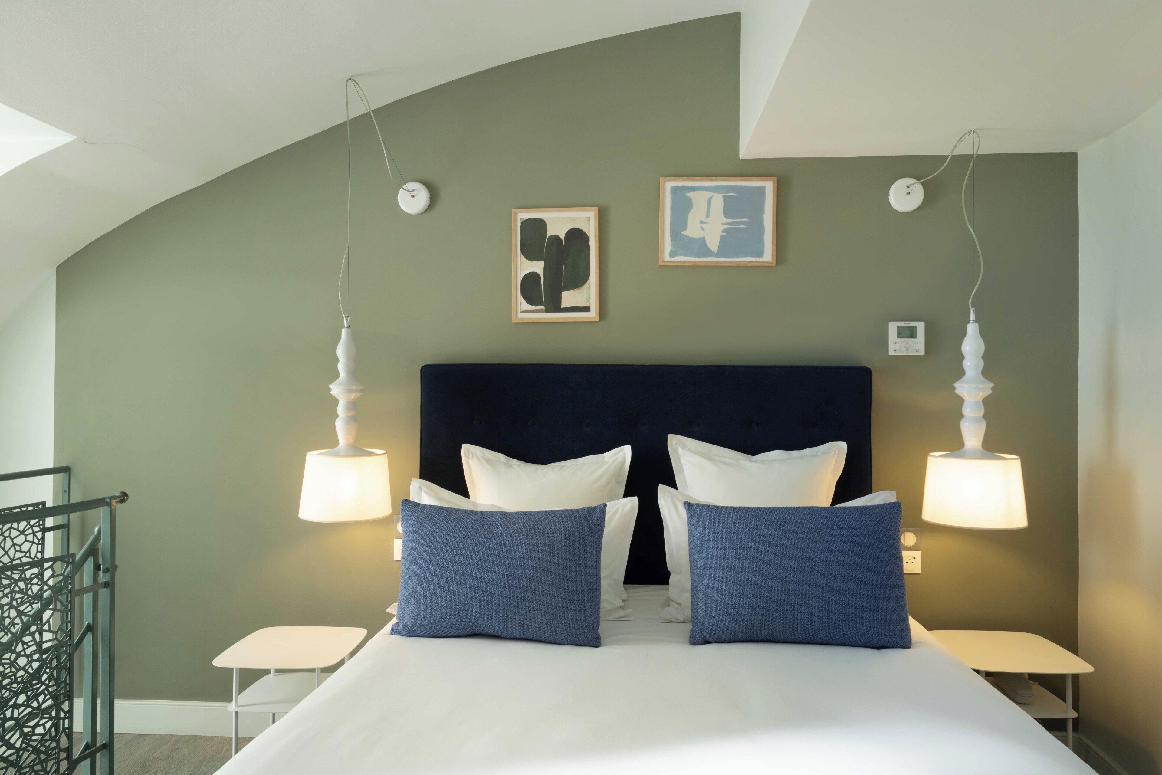 A bedroom with a curved ceiling, a dark headboard, two bedside tables, a bed with white and blue bedding, and two wall-mounted lamps.