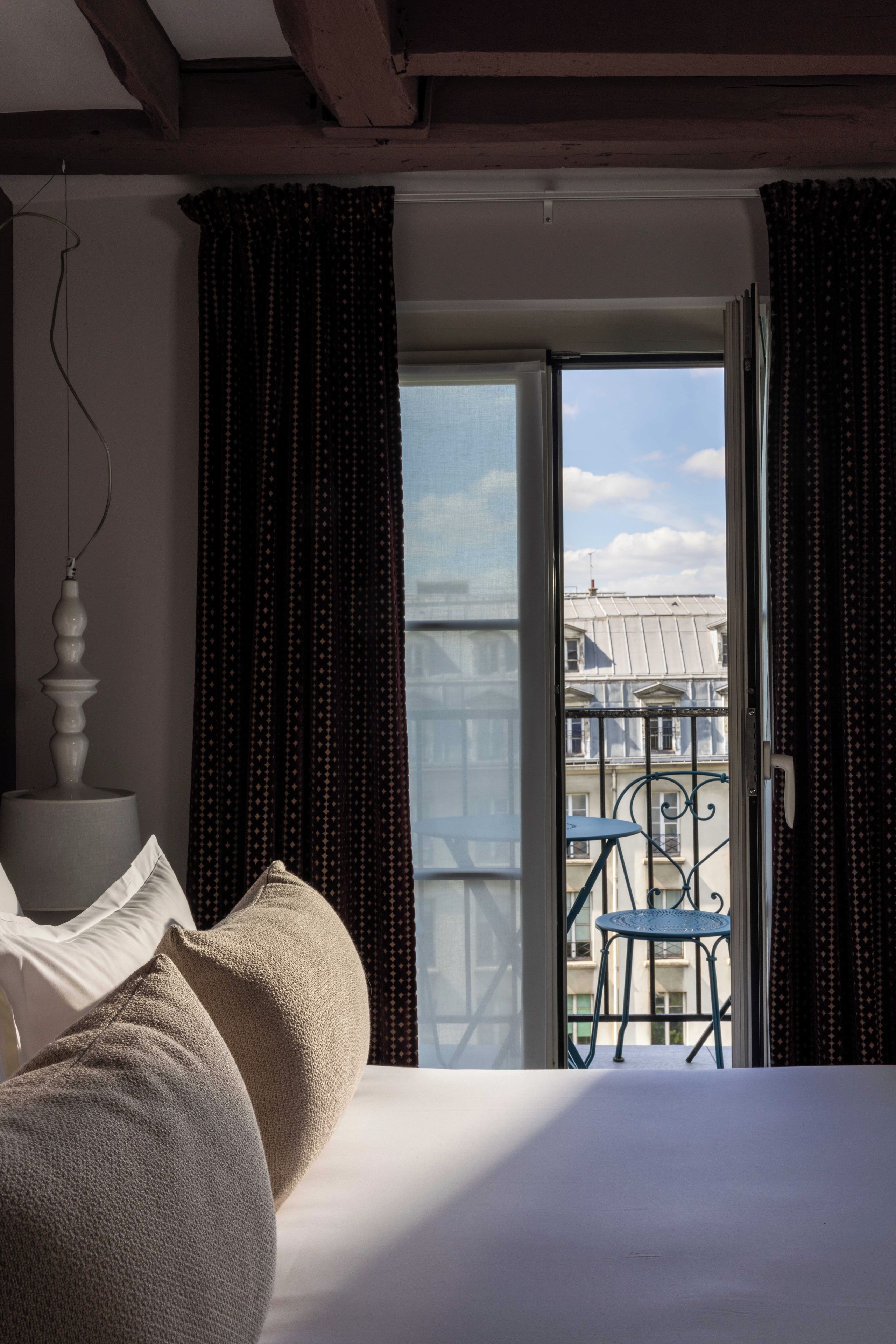 Une chambre à coucher comprenant un lit, une table de chevet, une fenêtre avec des rideaux et une vue sur un balcon avec une chaise.