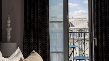 Ein Schlafzimmer mit einem Bett, einem Nachttisch, einem Fenster mit Vorhängen und Blick auf einen Balkon mit einem Stuhl.