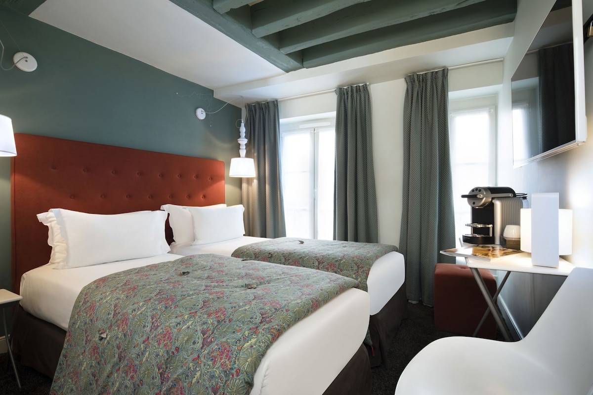 Una camera d'albergo con due letti, una scrivania con macchina del caffè e televisore.