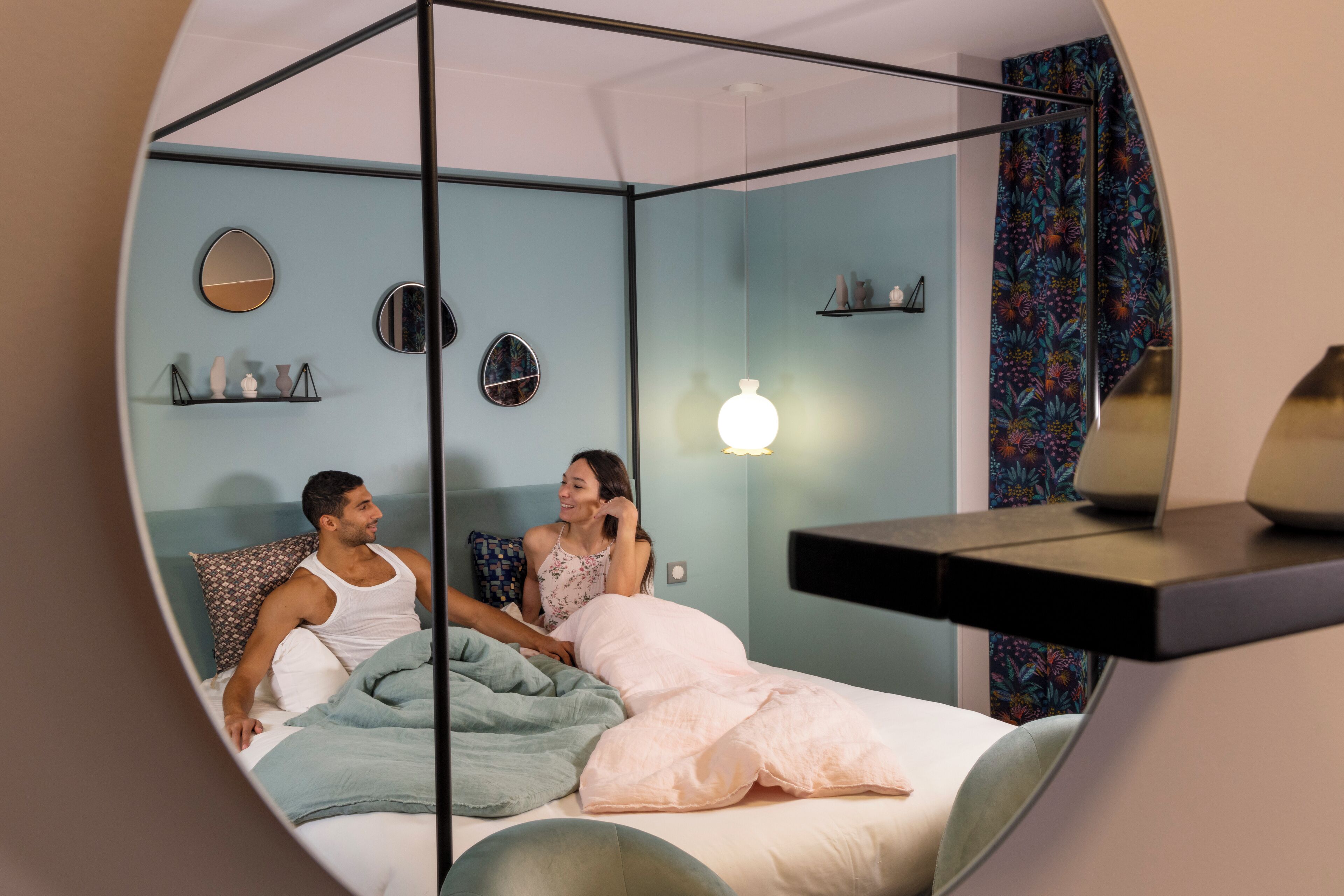 Une chambre à coucher avec un lit à baldaquin, une table de chevet, un miroir et une étagère murale agrémentée d’objets décoratifs.