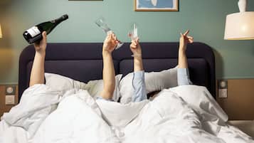 Une personne allongée dans un lit, avec des coupes à champagne et une bouteille à proximité.