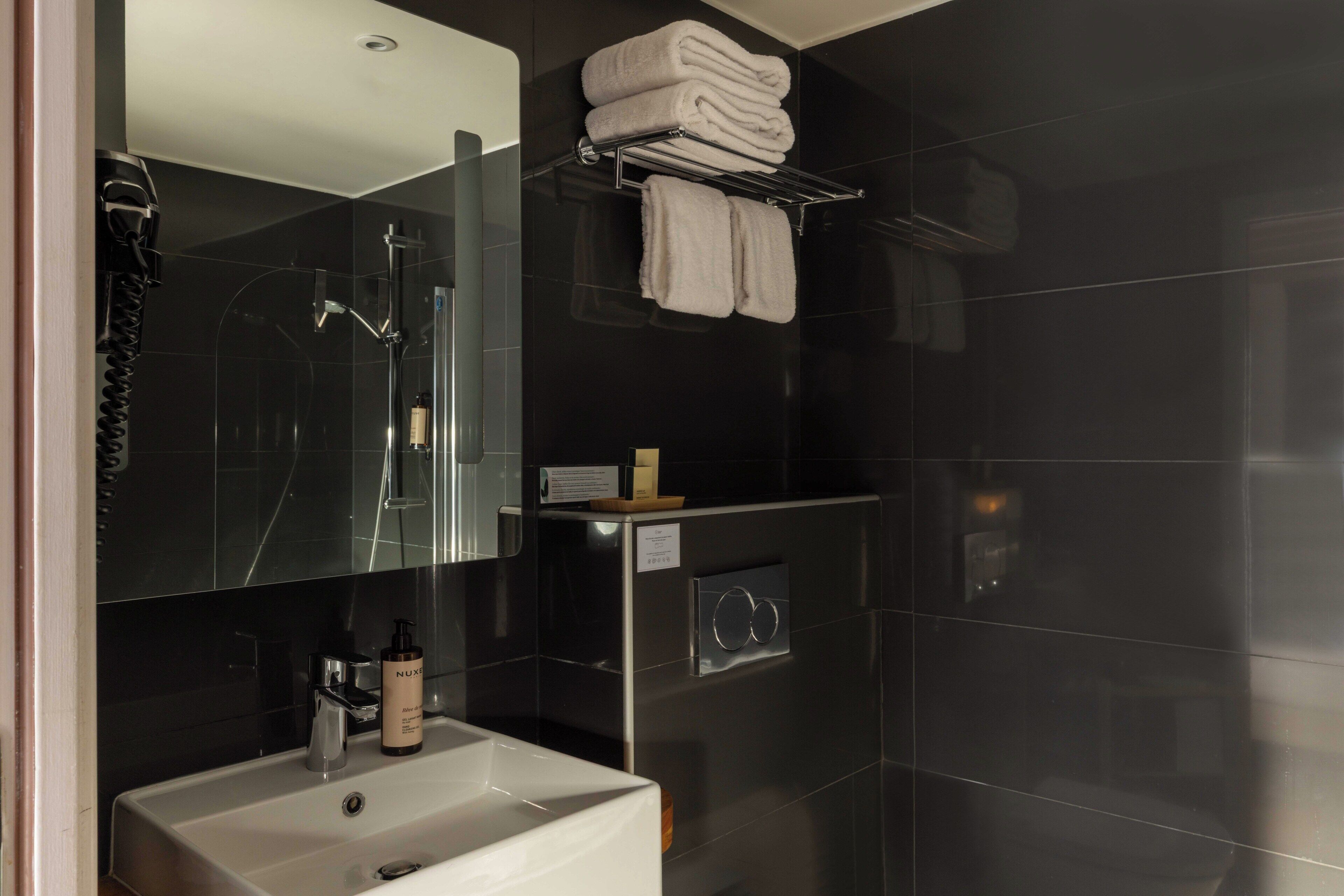 A modern bathroom with a glass shower enclosure, a sink with a mirror, and a towel rack with folded towels.