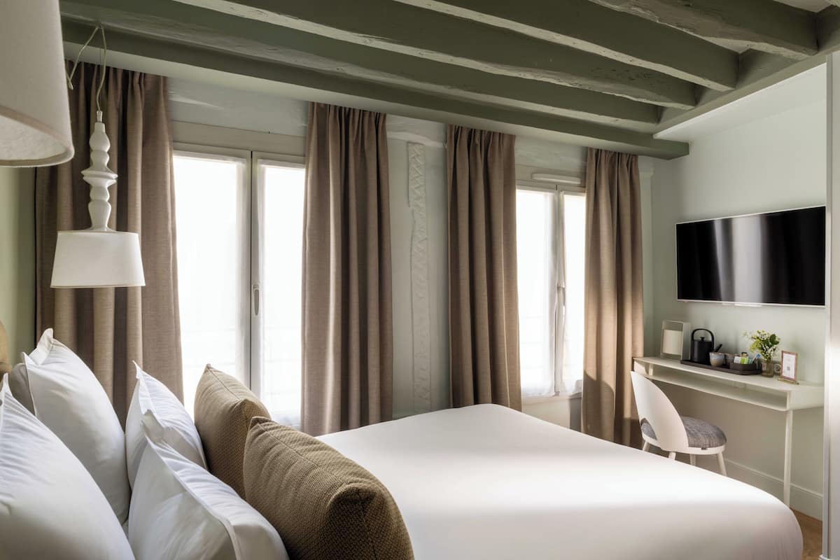 A hotel room with a bed, a desk, a chair, a television, and curtains.