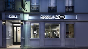 Facciata di un hotel con un evidente cartello 'HOTEL' e un cartello 'MARAIS HÔME' sopra l'ingresso.