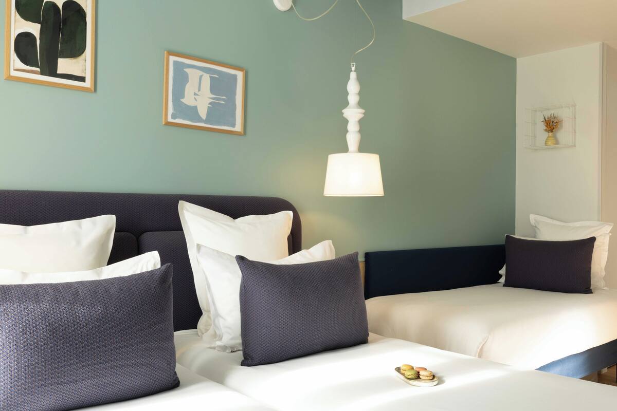 A hotel room with two beds, a hanging lamp, and artwork on the walls.