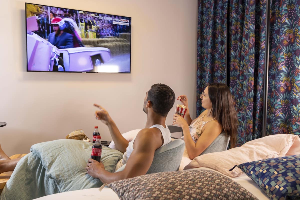 A room with a bed, a television mounted on the wall, and a patterned curtain.
