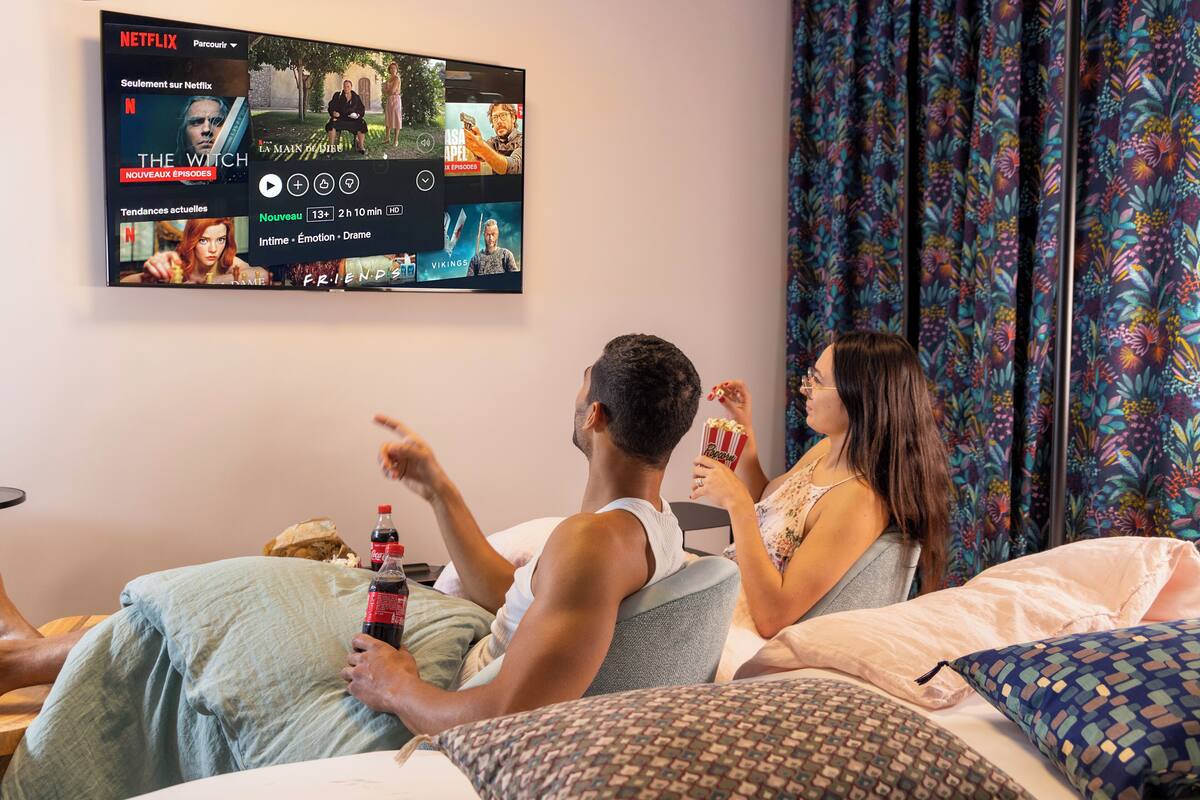 A bedroom with a large TV mounted on the wall displaying a Netflix interface.