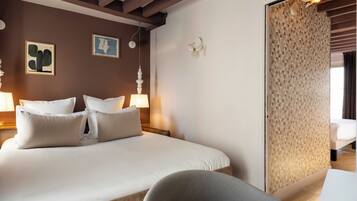 A hotel room with a large bed, two bedside tables with lamps, a chair, a wall with geometric patterned wallpaper, and a door leading to another room.