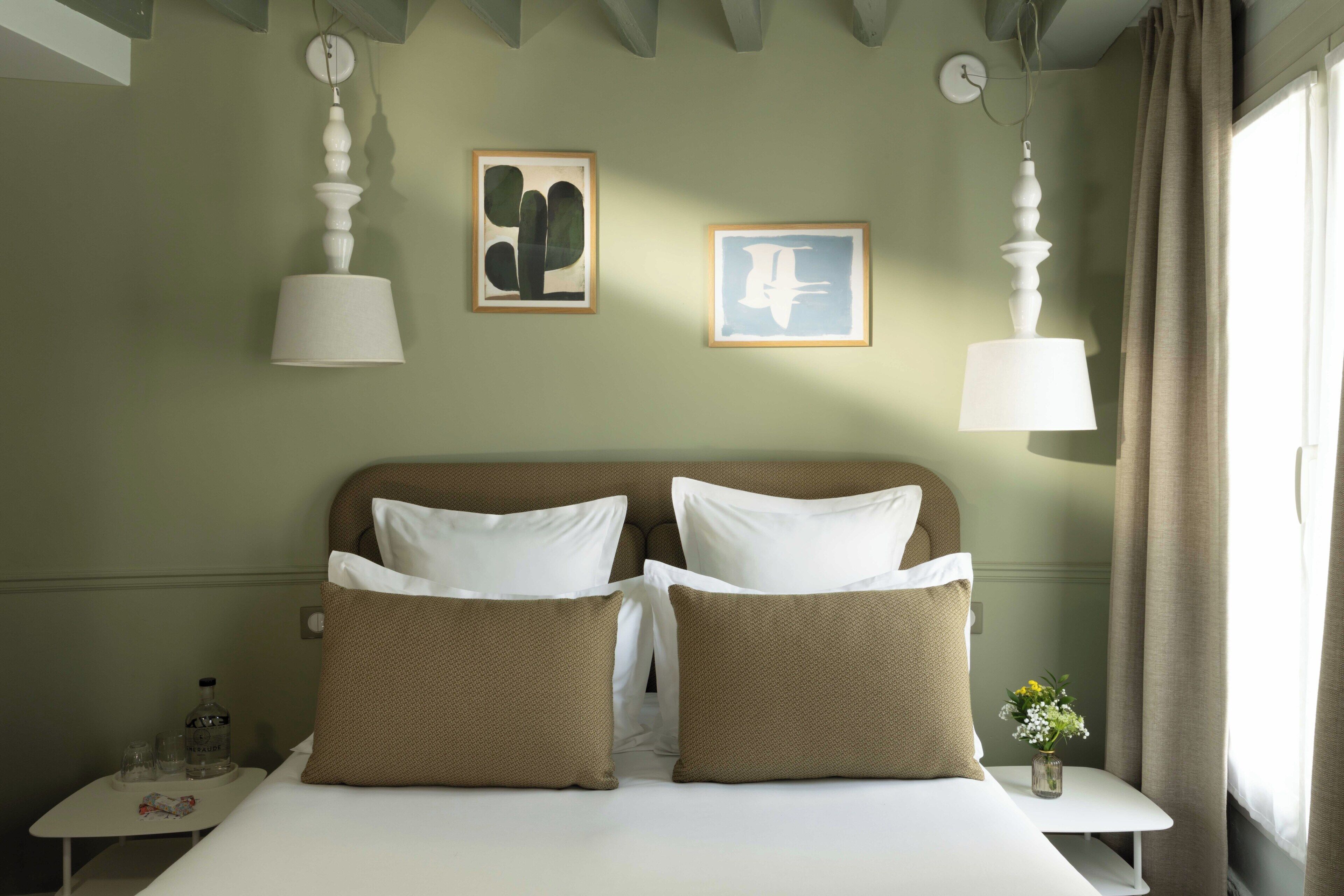 A hotel room with a bed, two pillows, a nightstand, a vase with flowers, and two wall art pieces.