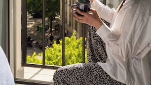 Une personne est assise sur un balcon, en train de lire un menu, avec une vue sur des bâtiments et de la verdure.