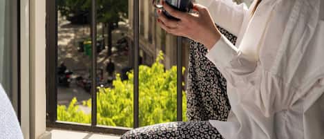 Une personne est assise sur un balcon, en train de lire un menu, avec une vue sur des bâtiments et de la verdure.