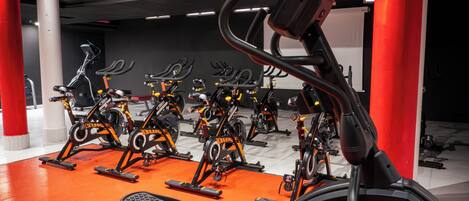 A gym with multiple stationary bikes and treadmills, red pillars, and a tiled floor.