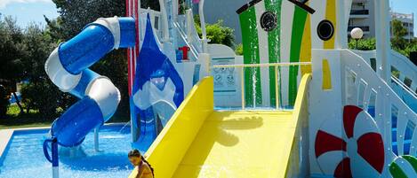 Parque acuático con un tobogán amarillo, uno azul y blanco, y una zona de piscina.