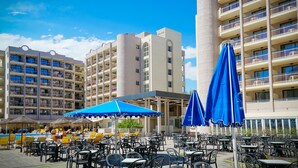 Un hotel con terraza al aire libre y sombrillas, varios pisos y una zona de piscina.