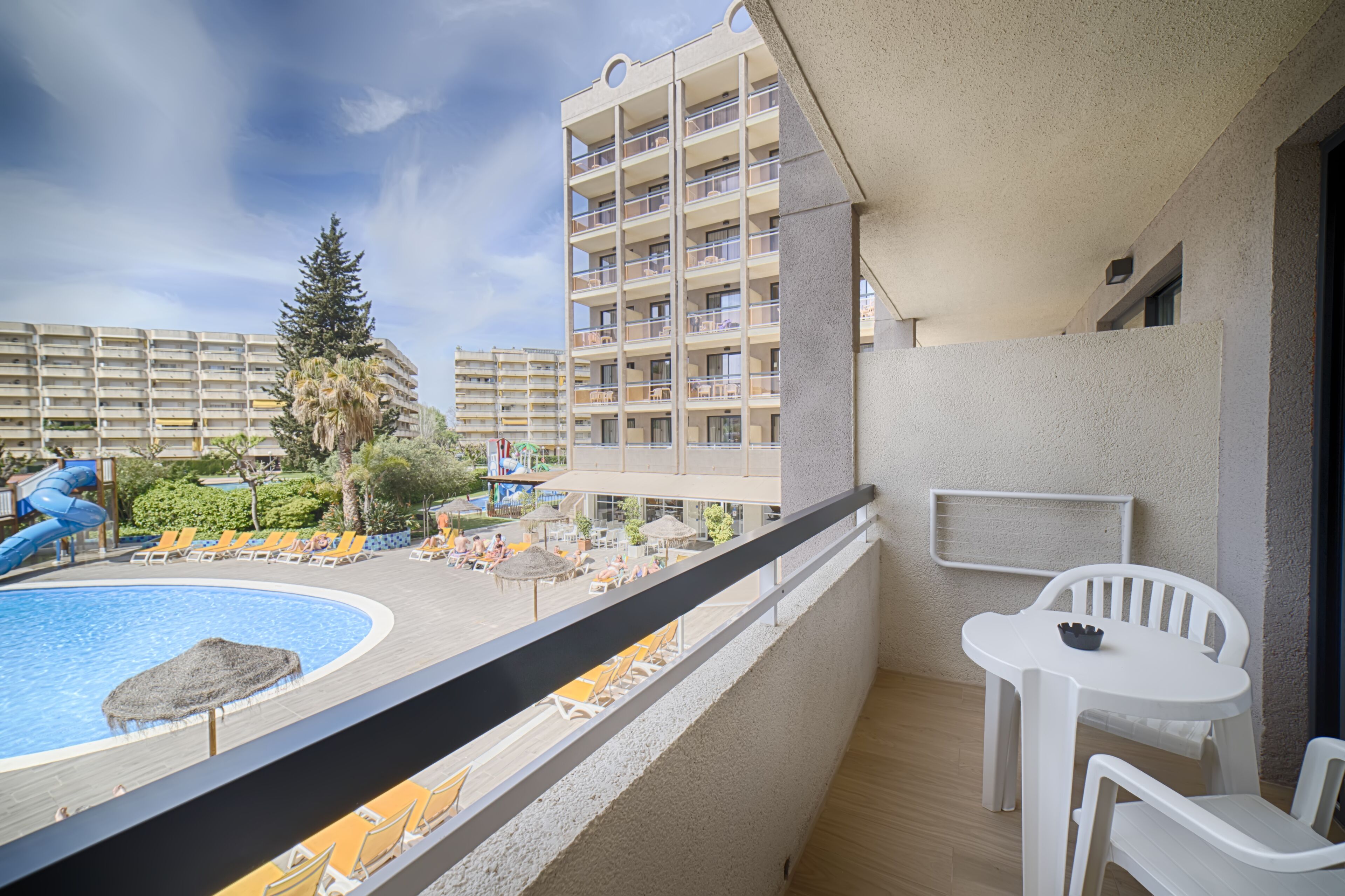 A balcony with a pool, lounge chairs, and a table.