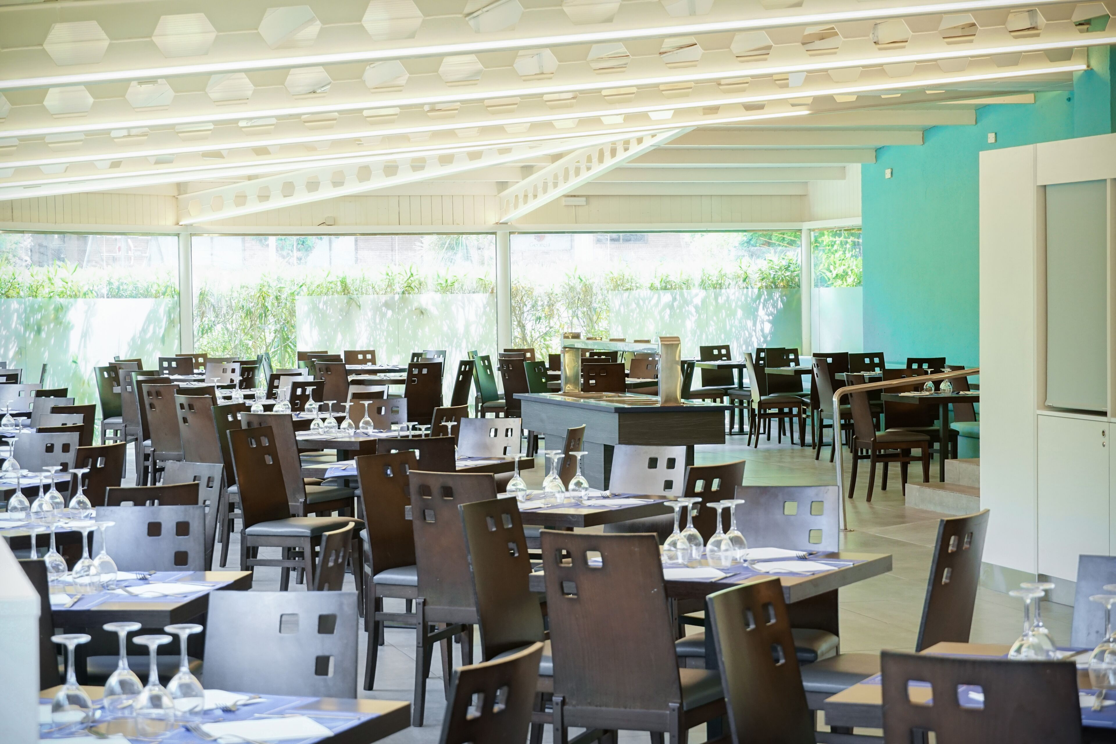 Een ruime restaurantruimte met meerdere tafels en stoelen, grote ramen en een modern plafondontwerp.
