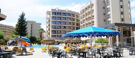 A resort pool area with outdoor seating and umbrellas, surrounded by buildings.