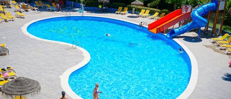 Una gran piscina con tobogán, rodeada de tumbonas y sombrillas.