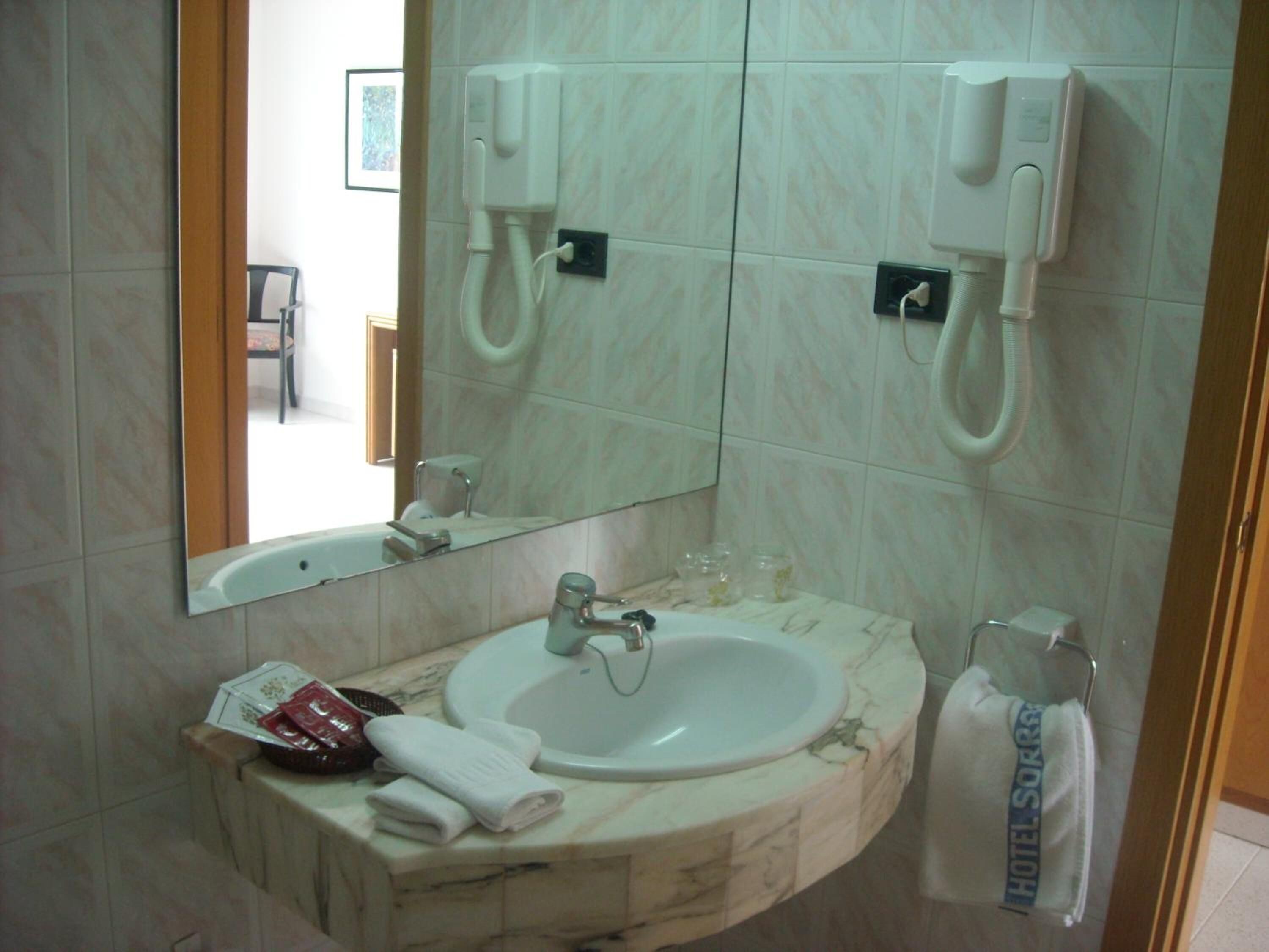 A bathroom with a marble sink, a mirror, two wall-mounted phones, and a towel rack.