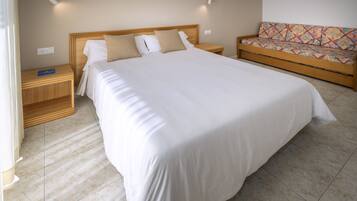 A hotel room with a large bed, a wooden nightstand, a sofa, and a wall-mounted light fixture.