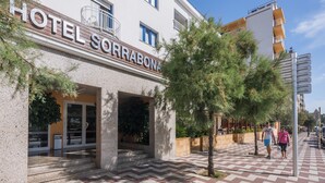 Ein Hotel namens "HOTEL SORRABONA" mit moderner Fassade, einem Außenbereich mit Sitzgelegenheiten und einem schachbrettartig gemusterten Gehweg.