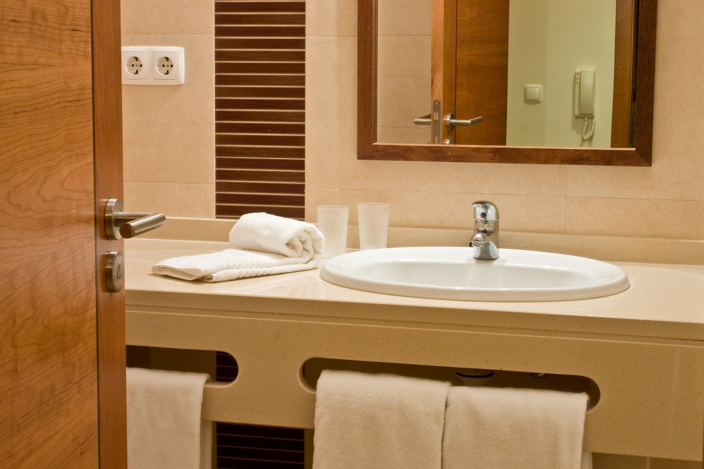 Un baño con lavabo, espejo, toallero y una puerta de madera.