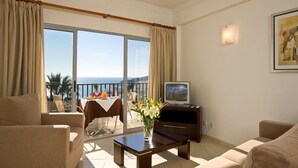 A living room with a sofa, a coffee table, a TV, and a balcony with a table and chairs. - Apartamentos Silmar (Albufeira)