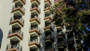 A multi-story building with balconies, a clear sky, and a tree with pink flowers. - Dorisol Buganvilia Studio Hotel (Funchal)