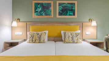Una cama doble con cabecera de madera, dos mesitas de noche con lámparas y dos láminas enmarcadas con motivos botánicos en la pared.