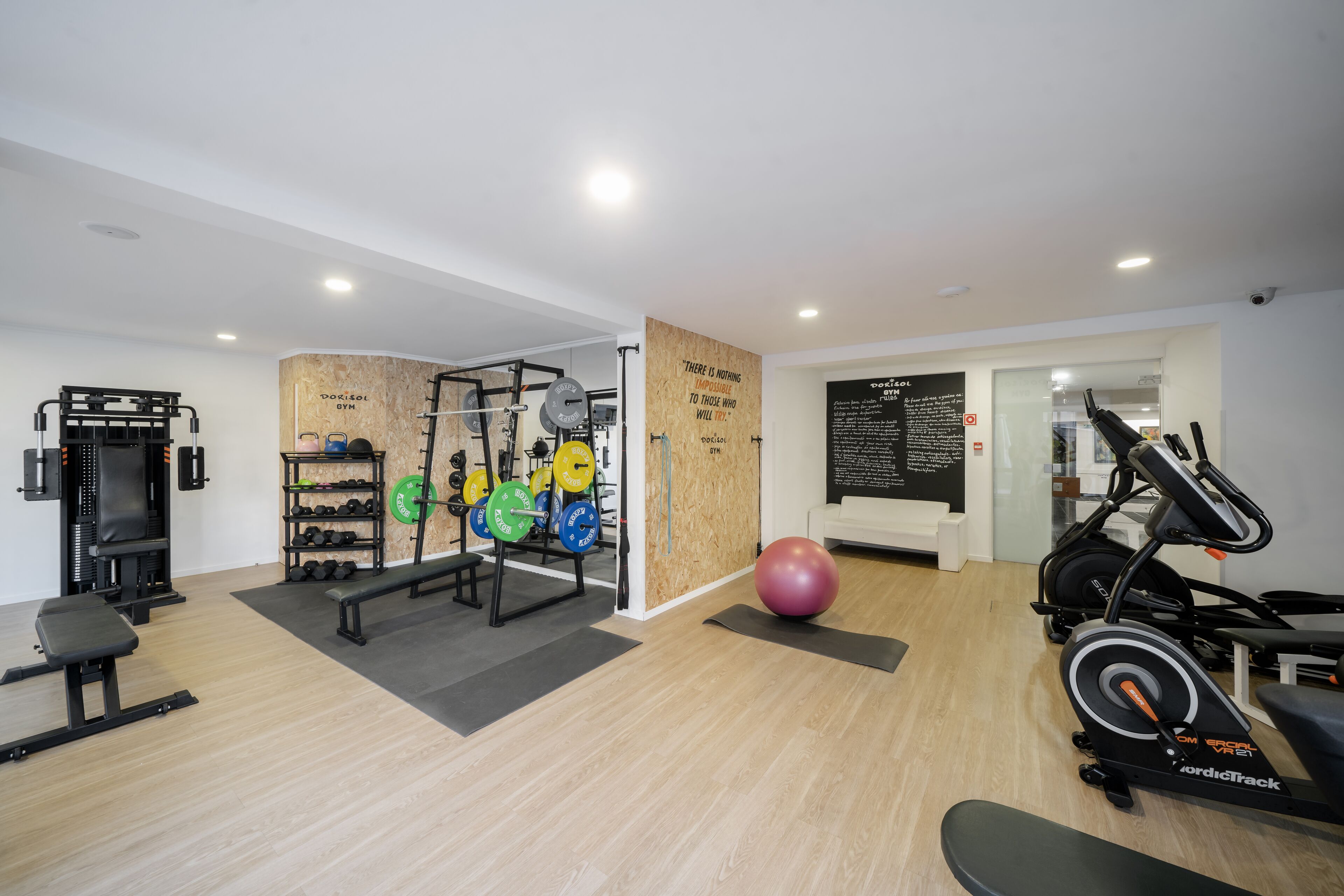 A modern gym with weightlifting equipment, cardio machines, and a motivational quote on the wall.