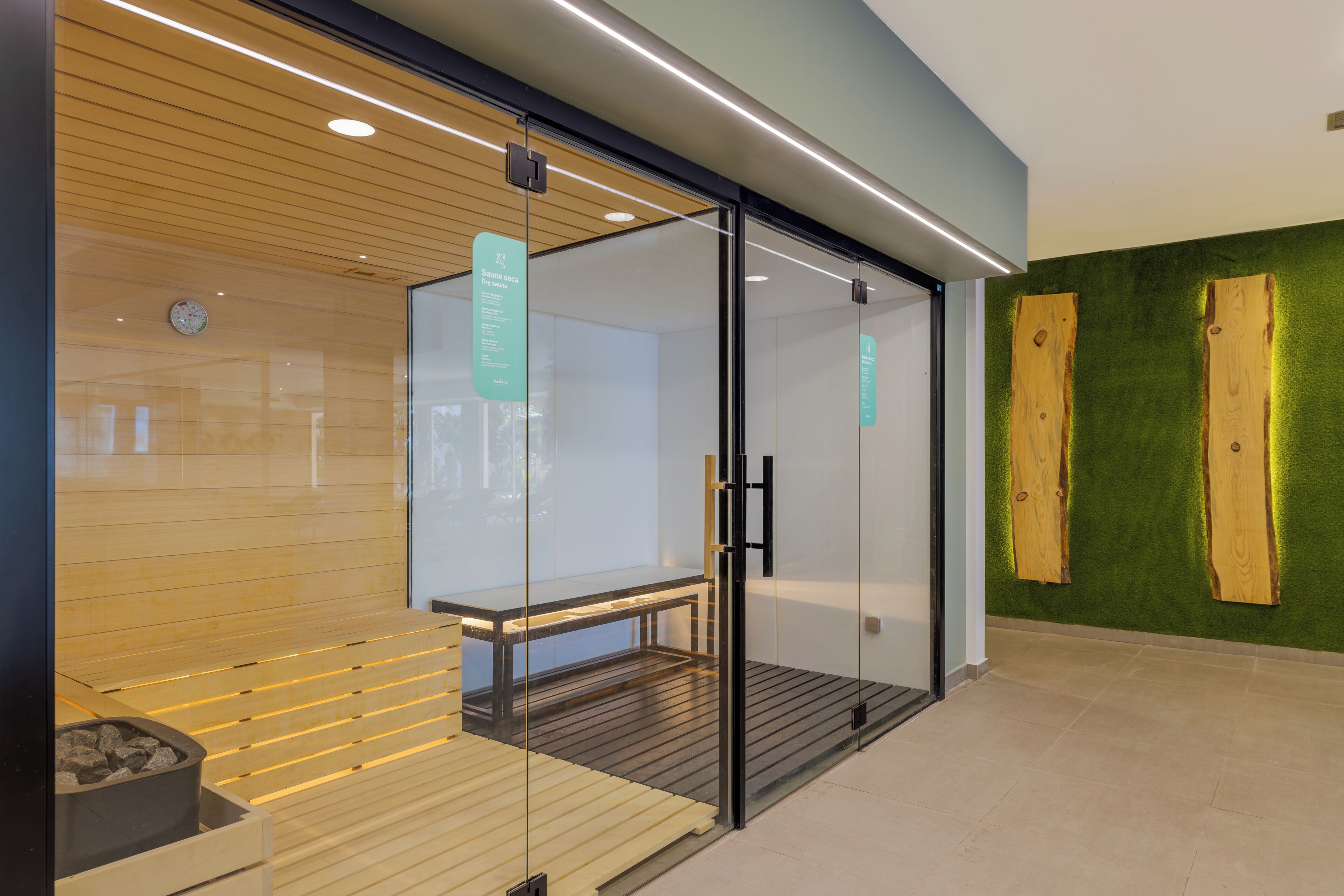 A dry sauna with glass doors, a wooden bench, and a wall-mounted sauna sign.