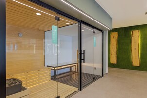 Una sauna asciutta con porte in vetro, una panca in legno e un cartello a muro.