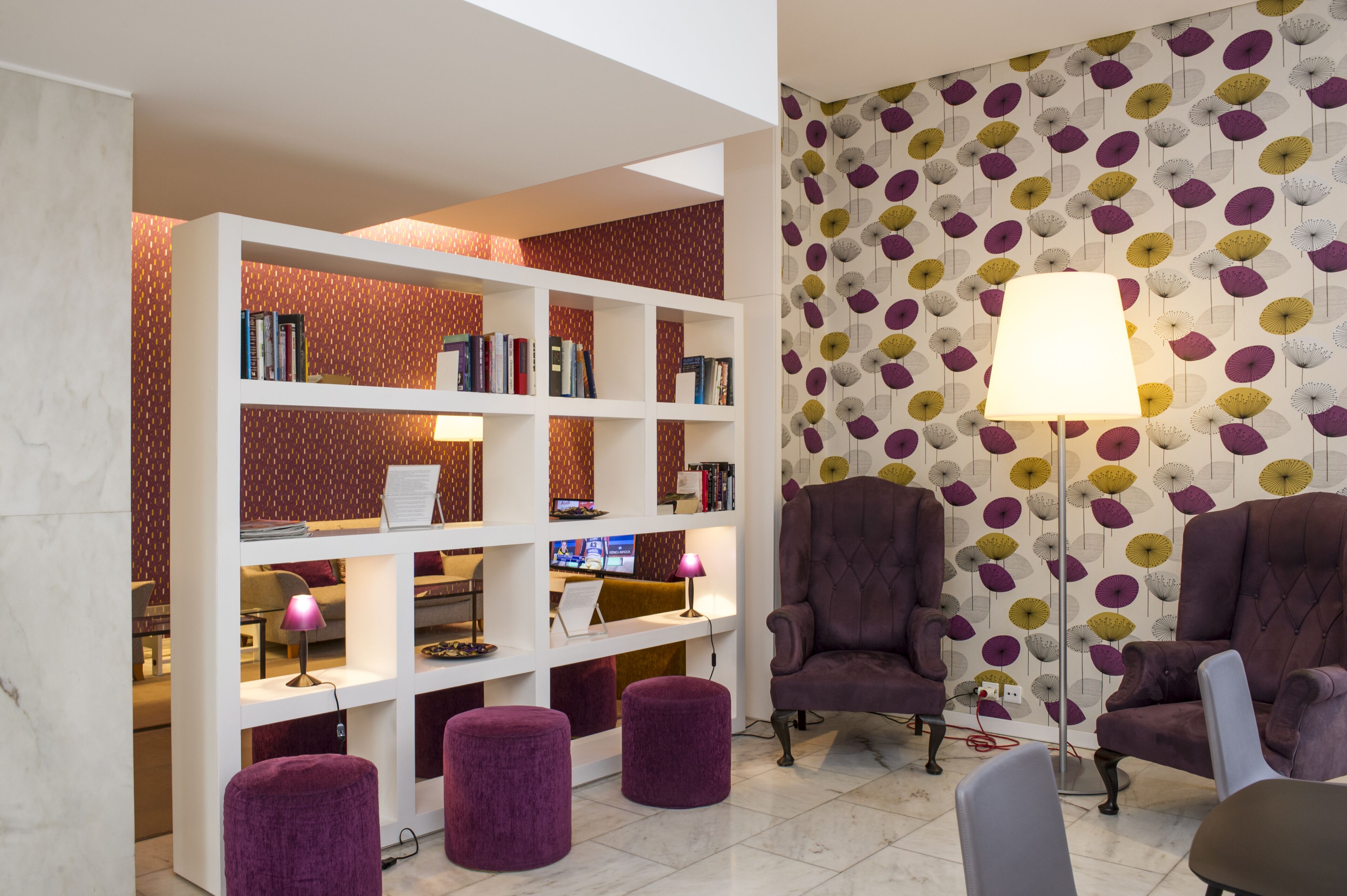 Ein modernes Wohnzimmer mit einem weißen Bücherregal, violetten Ohrensesseln und einem gemusterten Wandpapier.