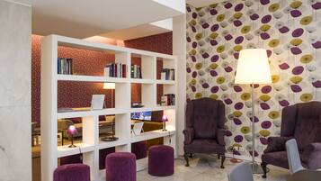 Ein modernes Wohnzimmer mit einem weißen Bücherregal, violetten Ohrensesseln und einem gemusterten Wandpapier.