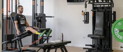 A gym with exercise equipment, a bench, and a television on the wall.