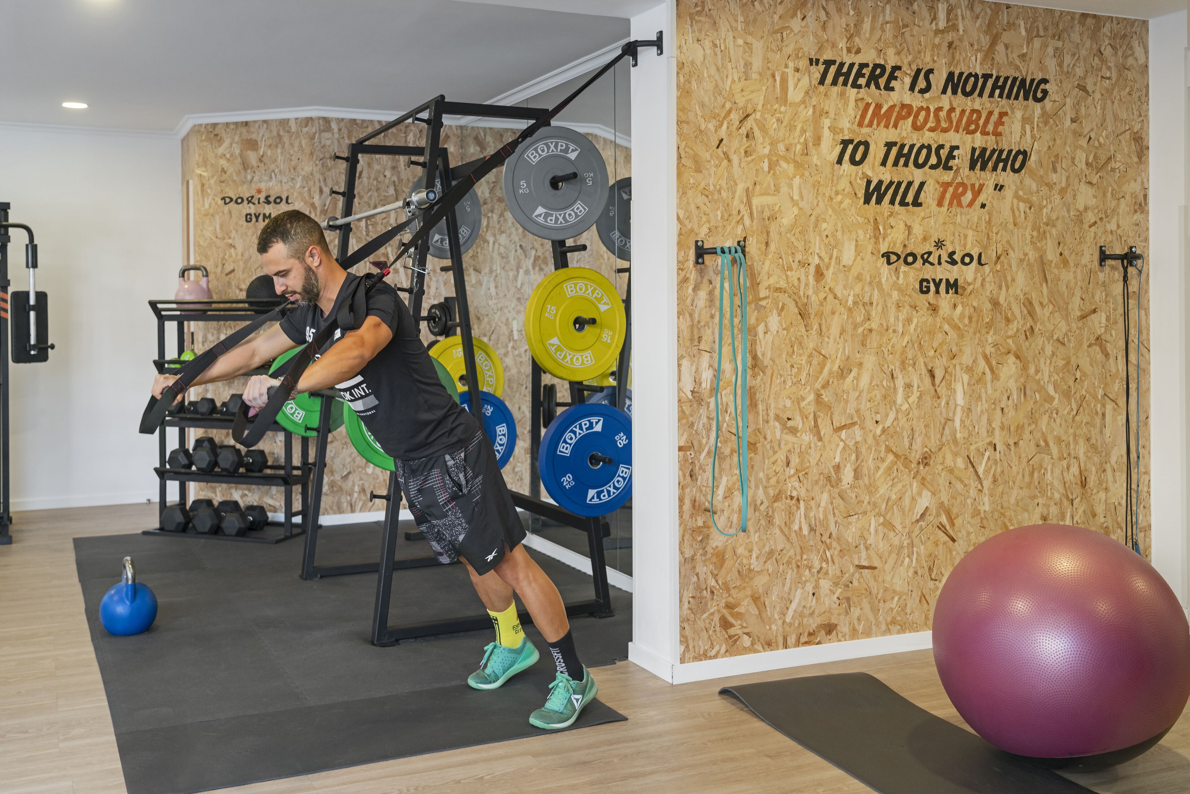 A gym with weightlifting equipment, a motivational quote on the wall, and exercise balls.