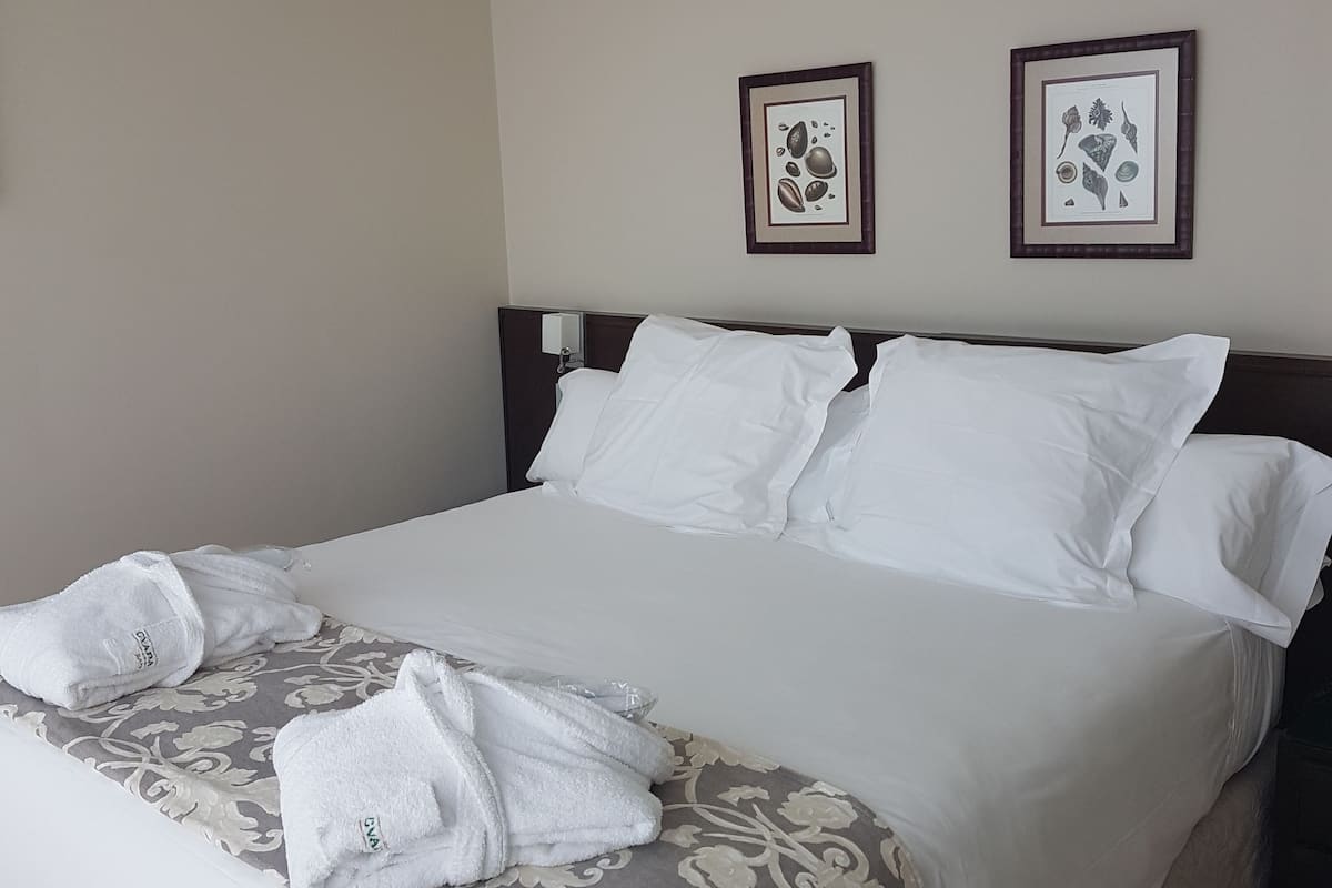 A neatly made bed with white linens and a patterned bedspread, two framed wall art pieces, and a bedside table with a lamp.