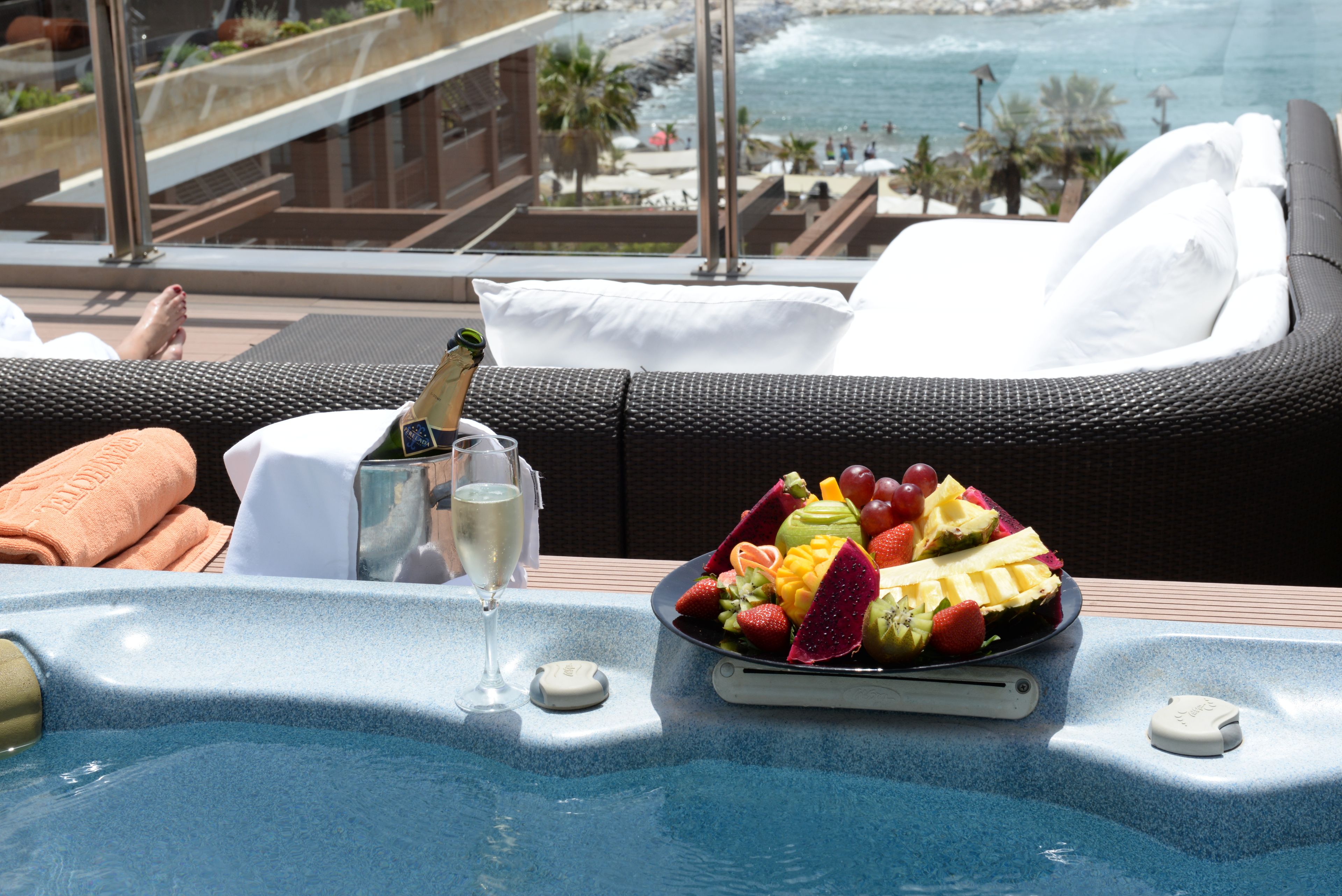 Escena junto a la piscina con un jacuzzi, una bandeja de frutas y una copa de champán.
