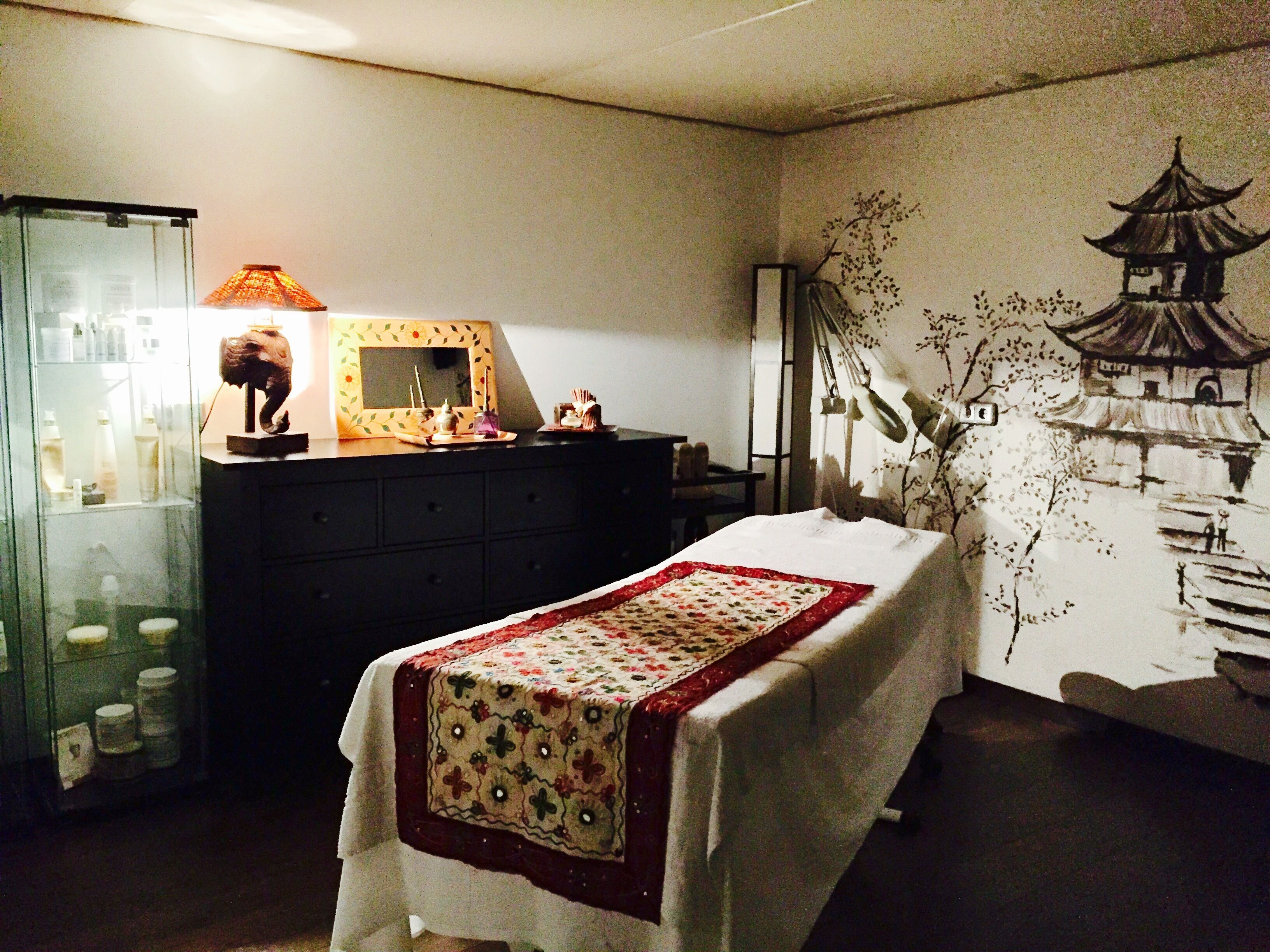 A bedroom with a bed, a dresser, a mirror, and a wall with a mural.