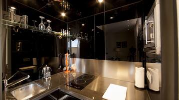 Een moderne keuken met roestvrijstalen apparatuur, een glazen plank met flessen en een grote spiegel die de kamer weerspiegelt.